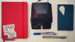 tools for documentation include a Polaroid Now+ camera; a red notebook with a sticker of Alexis Rose from Schitt's Creek saying, I love this journey for you; a blue notebook with a sticker reading, you are here; a micron pen; and a blue gel-ink pen.
