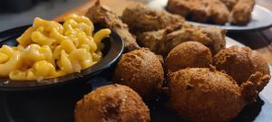 a dinner plate with fried chik’n and hush puppies, and a cup of mac and cheese, with another plate of mozzarella sticks and marinara in the background