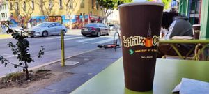 A Philz coffee cup on a cafe table outside the shop. 24th Street in the Mission is faded in the background.