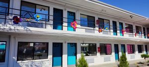 The exterior of Hotel Zazz, a mid-century-style motel in Albuquerque. There are two stories, with a white facade, turquoise doors, and bold-colored artificial flowers decorating the railing.