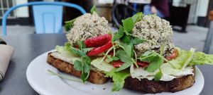 an open-faced vegan-tuna sandwich, with two scoops of tuna top a bed of lettuce and tomato on slices of thick, hearty bread